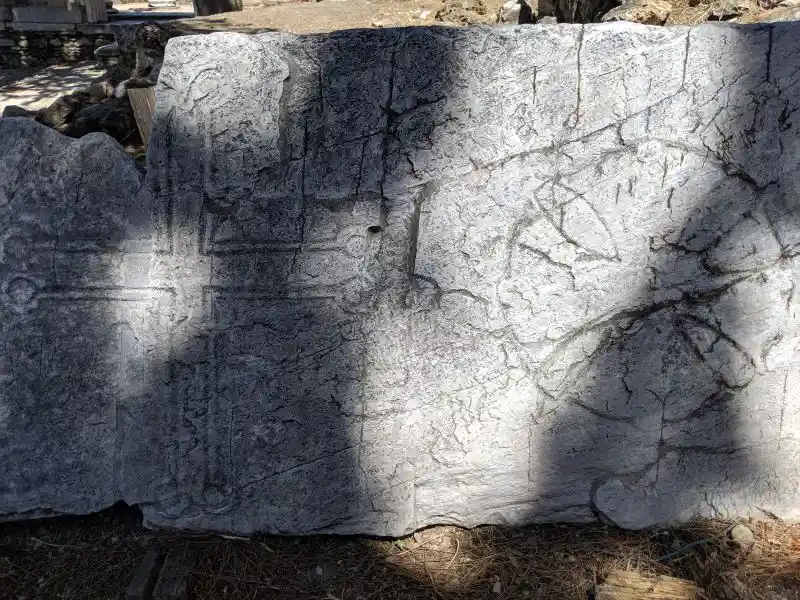 Weathered archaeological slab featuring cross and circular emblem in shaded terrain